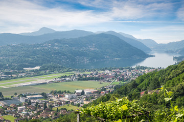 Fototapeta na wymiar Lake Lugano, Switzerland. Picturesque aerial view of the town of Agno, lake Lugano, Lugano airport on a beautiful summer day. Agno is a municipality in the district of Lugano in the canton of Ticino