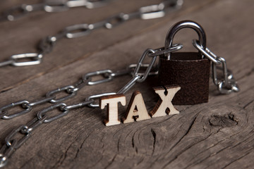 The word TAX next to the chain and the closed lock on an old wooden background.