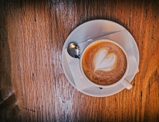hot cappuccino coffee with heart shaped froth on wooden table
