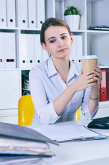 Tired and exhausted woman looks at the mountain of documents holding a paper glass with coffee in hands.