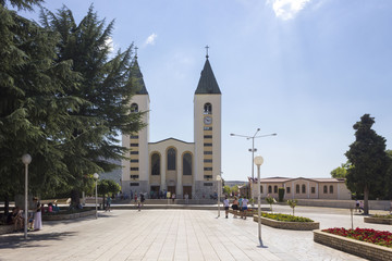 Fototapeta na wymiar Frontal view of Saint James church in Medjugorje, with few people around the square