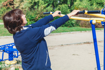 elderly woman performs exercises on simulators on summer sports ground