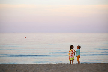 children boy and girl romance on the seashore colorful sunset.