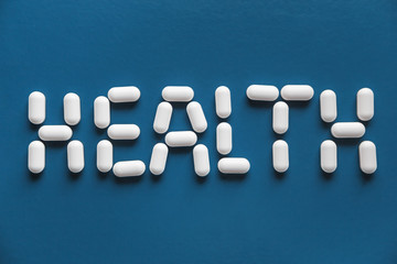 White pills with inscription HEALTH on blue surface background