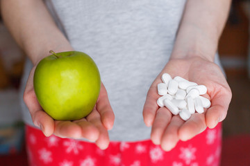 Woman holds a green apple in one hand and a handful of pills in the other.
