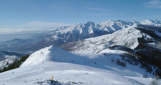 Forward aerial top view over winter snowy mountain and ski track field with people in sunny day.Alps mountains snow season establisher.4k drone flight establishing shot