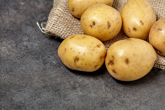 Raw potato on black wood table in kitchen. Preperation for cooking.