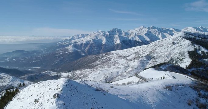 Forward aerial top view over winter snowy mountain and ski track field in sunny day.Revealing valley.Alps mountains snow season establisher.4k drone flight establishing shot