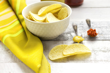 potato chips on white glass bowl with spoons of mustard and red pepper