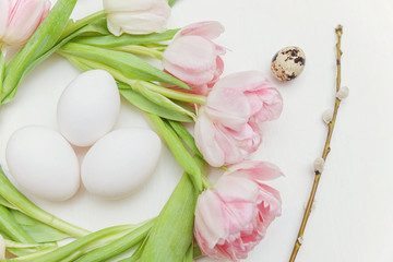 Obraz na płótnie Canvas Spring greeting card. Easter eggs in the nest of tulips on white wooden background. Easter concept. Flat lay. Spring flowers tulips