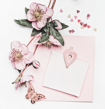 Lovely pastel pink layout with flowers decoration,ribbon, hearts and card mock up on white desk background, top view, flat lay. Wedding invitation, girls birthday or Mother Day greeting concept