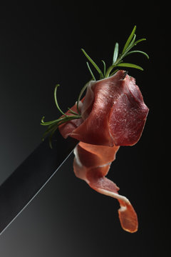 Prosciutto with rosemary on a knife blade.