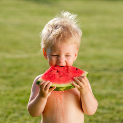 One year old baby boy eating watermelon in the garden
