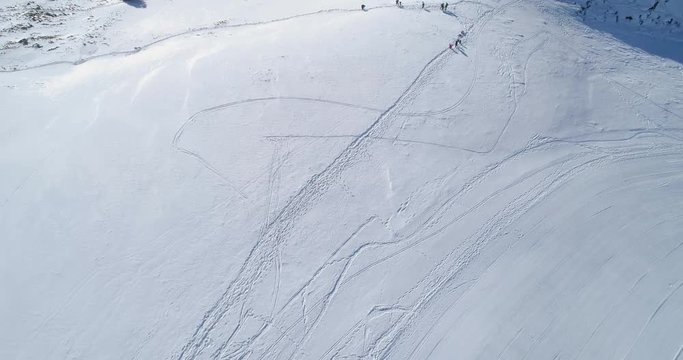 Backward aerial top view over winter snowy mountain ski track field with people in sunny day.Above Alps mountains snow season establisher.4k drone flight establishing shot