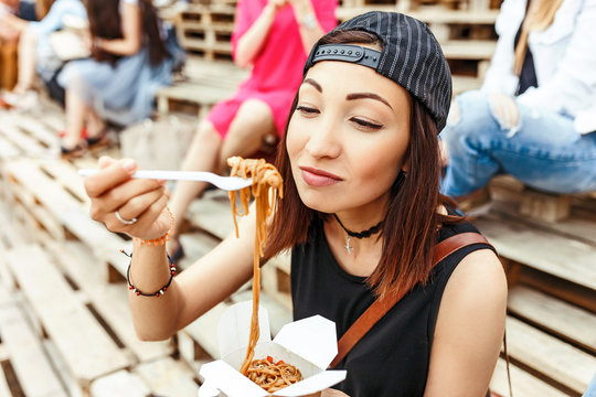 Portrait of happy smiling young woman eating Asian noodles outdoors, fastfood concept