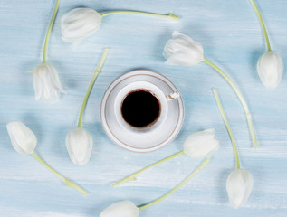 cup of coffee on a table with white tulips. Top view.