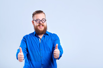 A fat, bearded man with glasses on a gray background with a positive stupid expression of emotion.