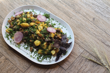 Fried beef with potato, greens and onions on a wooden background
