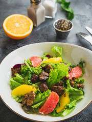 Tasty salad with citrus, lettuce and grilled chicken liver in a plate.