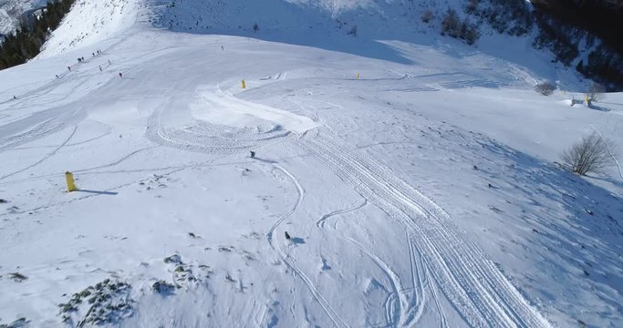aerial follow over skier alpine skiing with dog running behind in winter snowy mountain ski track field in sunny day.Above Alps mountains snow season active ski sport people.4k drone flight