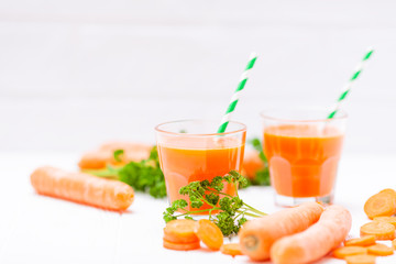 Carrot juice in beautiful glasses, cut orange vegetables and green parsley on white wooden background. Fresh orange drink. Close up photography. Selective focus. Horizontal banner
