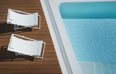 View from above of two white canvas chaise lounge chairs positioned by a turquoise infinity pool, holiday concept, traveling  to an exotic destination, working from home, or luxury home ownership 