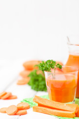 Carrot juice in beautiful glasses, cut orange vegetables and green parsley on white wooden background. Fresh orange drink. Close up photography. Selective focus. Vertical banner