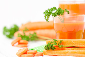 Carrot juice in beautiful glasses, cut orange vegetables and green parsley on white wooden background. Fresh orange drink. Close up photography. Selective focus. Horizontal banner