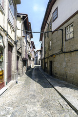 Narrow lonely alley with uneven cobblestone floor and Gothic style houses with stone facades in a village in Portugal called Guimaraes