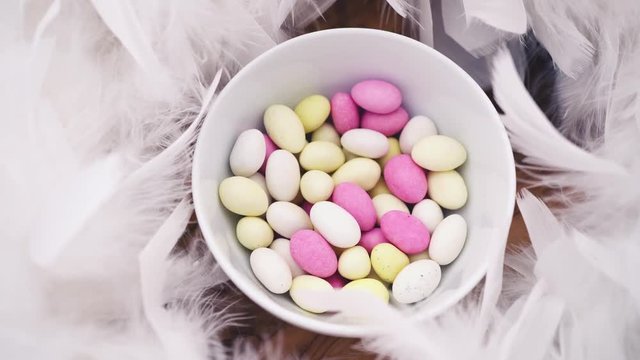 small pastel easter egg candy in a bowl with white feathers turning slowly