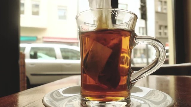 Dipping a teabag in a teaglass. Close up, low angle view Personal perspective. City people and traffic in the background.