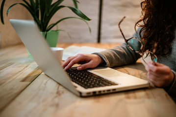 Closeup woman typing on laptop and holding glasses.