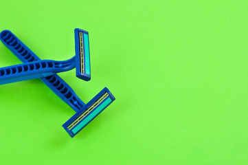 Two new blue plastic disposable razors with two blades and humid strip on blank green paper