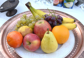 Fruits – bananas, apples, oranges and grapes, placed on a white plate.
