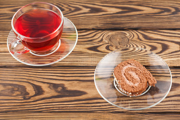 Full cup of red tasty raspberry tea and slice of roll pie on glass saucer on old wooden rustic table