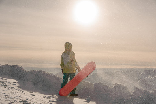 Snowboarder in sportswear standing on the background of the mountain peaks and sun
