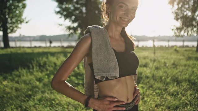 Woman showing slim abdomen after training outdoors on sunny day.