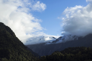 Obraz na płótnie Canvas Paisaje de picos de montañas nevados y verdes con cielo nublado en Nueva Zelanda