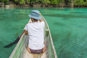 Tourist paddling on traditional wooden canoe on blue lagoon in the remote Togean Islands, Central Sulawesi, Indonesia.