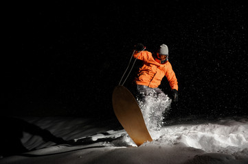 Male snowboarder in orange sportswear balancing on the snowboard at night