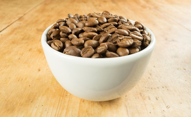 Lightly roasted brown coffee beans in a white bowl on a wooden table