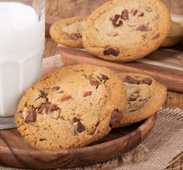 Chocolate chip cookies and glass of milk on a wooden plate