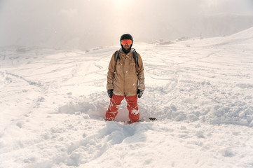 Male bearded snowboarder in sportswear and helmet standing on the snow hill