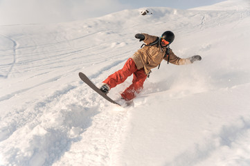 Male snowboarder in sportswear and helmet riding down the powder snow hill