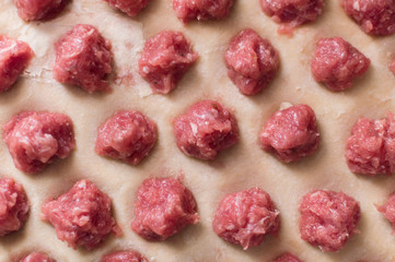 Meat balls laying on the rolled out wheat dough. Potstickers cooking.