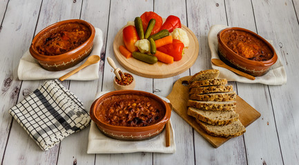 Cooked beans in clay pots, pickled vegetable and homemade bread on white wooden table