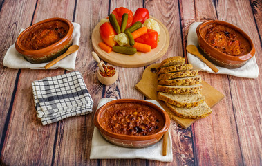 Cooked beans in clay pots, pickled vegetable and homemade bread on wooden table