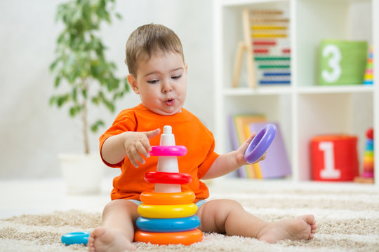 Baby plays sitting on floor. Educational toys for preschool and kindergarten child. Little boy building pyramid toys at home or daycare.