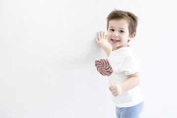 Fashion baby boy. Trendy boy with lollipop. funny cute little infant in white t-shirt. care of teeth, danger of tooth decay. Asian baby 2 years old. Happy kid with a big candy. Small child