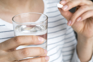 Close up image of woman putting white round pill in mouth. Sick female taking medicines, antidepressant, painkiller or antibiotic. Young lady drinking contraceptives. Pharmacy and healthcare concept